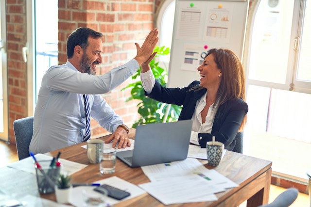 Two people in business dress high-fiving at a table.