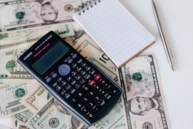 A calculator and a notepad sitting on top of some American money.